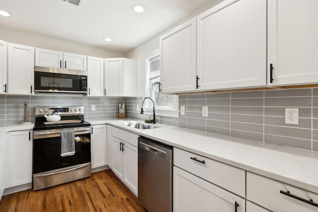 kitchen with a sink, backsplash, stainless steel appliances, white cabinetry, and dark wood-style flooring