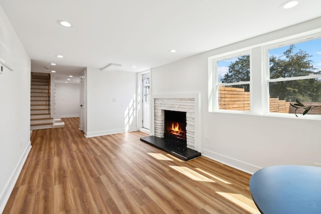 unfurnished living room featuring wood finished floors, baseboards, recessed lighting, a fireplace, and stairs