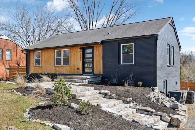 view of front of property with fence, brick siding, central AC, and a shingled roof