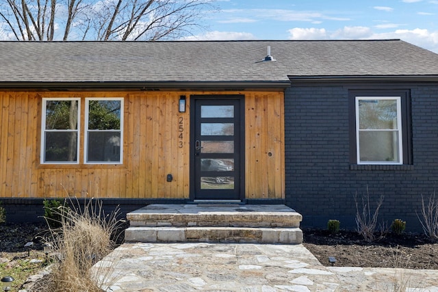 entrance to property featuring brick siding and a shingled roof