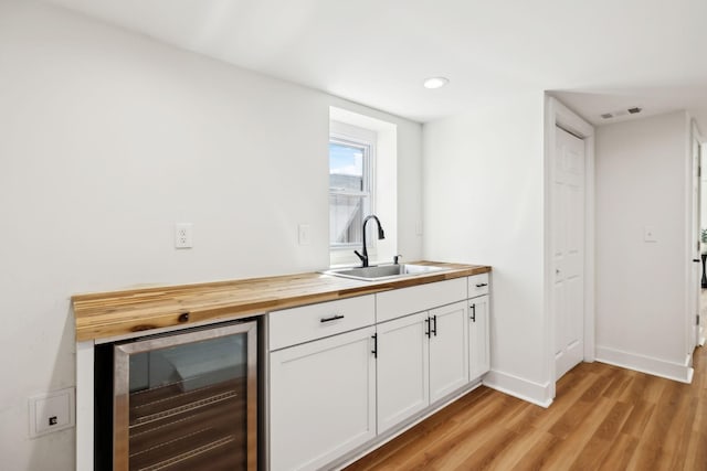 kitchen with light wood finished floors, wooden counters, a sink, wine cooler, and white cabinets