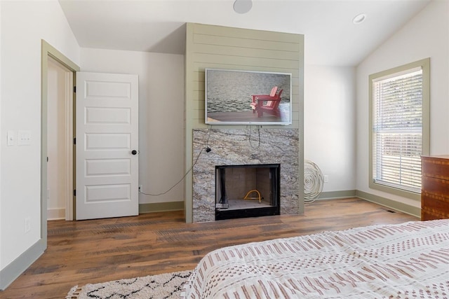 bedroom with vaulted ceiling, wood finished floors, baseboards, and a large fireplace