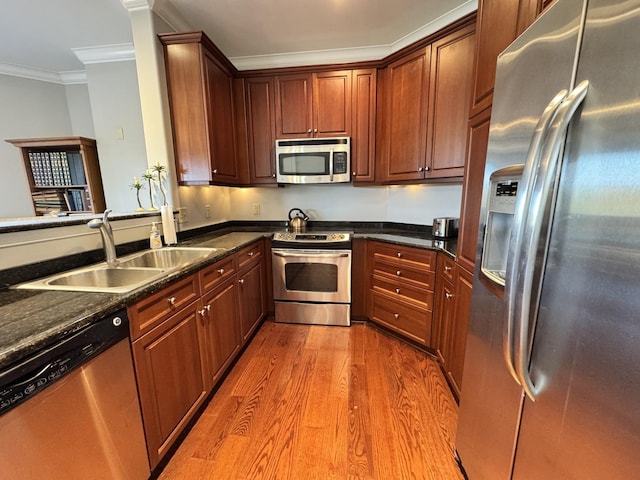 kitchen with dark stone counters, ornamental molding, wood finished floors, stainless steel appliances, and a sink