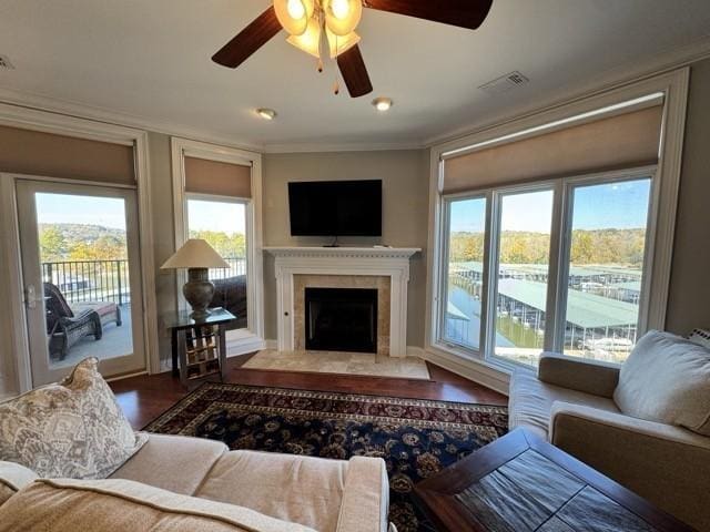 living room featuring wood finished floors, plenty of natural light, ornamental molding, and a fireplace with flush hearth