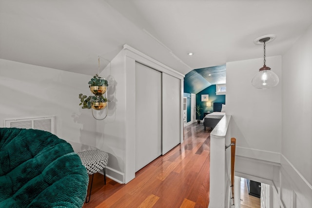 corridor with vaulted ceiling, an upstairs landing, light wood-style floors, and baseboards