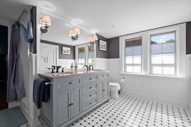 bathroom with double vanity, toilet, a wainscoted wall, and a sink