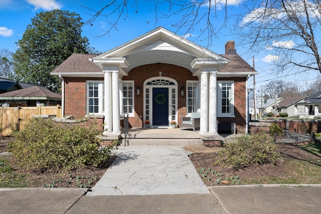 greek revival inspired property with brick siding, covered porch, a chimney, and fence