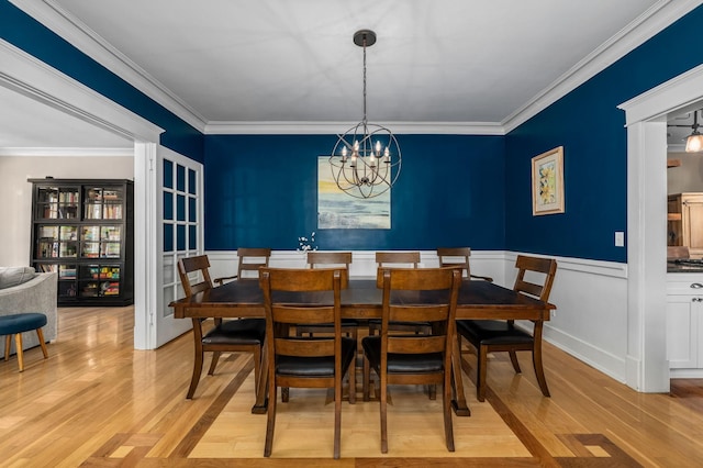 dining room with a chandelier, a wainscoted wall, light wood-type flooring, and ornamental molding