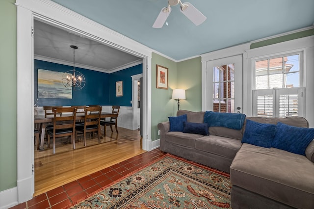 living room with dark tile patterned floors, ceiling fan with notable chandelier, baseboards, and ornamental molding