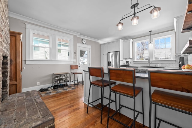 kitchen featuring a kitchen bar, dark countertops, stainless steel refrigerator with ice dispenser, and ornamental molding