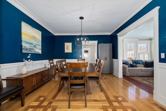 dining room featuring light wood-type flooring, ornamental molding, a wainscoted wall, and a chandelier