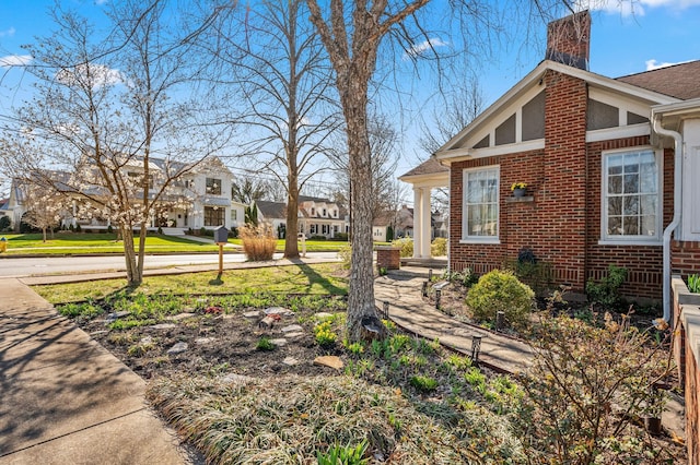 view of home's exterior with brick siding, a residential view, a chimney, and a yard