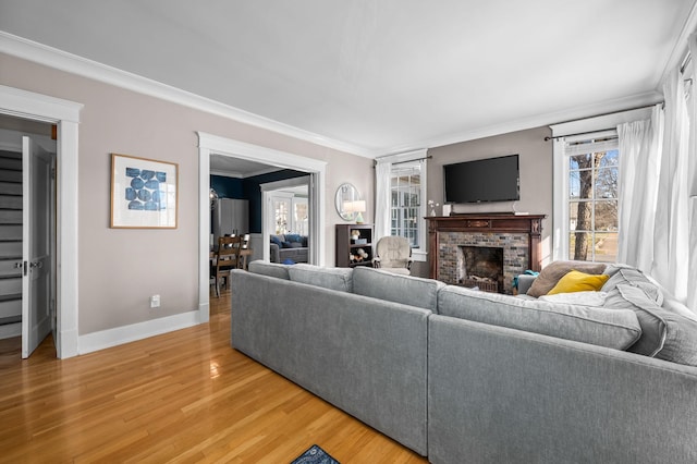 living area featuring a fireplace, baseboards, crown molding, and light wood-style floors