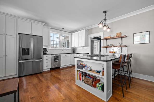 kitchen featuring dark countertops, open shelves, a kitchen breakfast bar, stainless steel appliances, and a sink