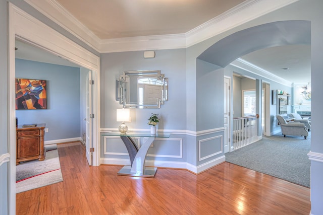 hallway featuring arched walkways, a wainscoted wall, wood finished floors, and ornamental molding