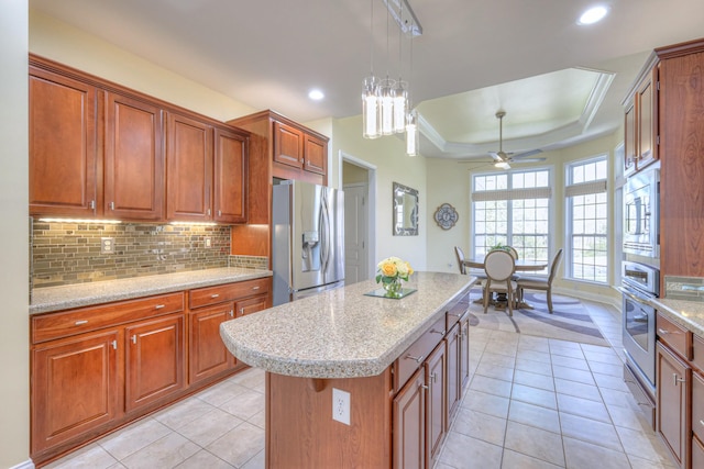 kitchen featuring a tray ceiling, stainless steel appliances, brown cabinets, and backsplash