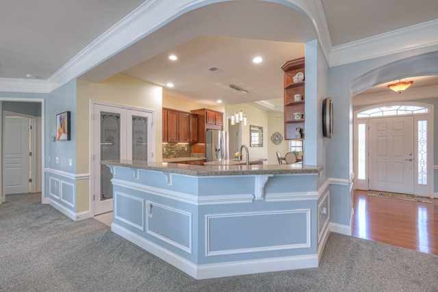 kitchen featuring brown cabinetry, a breakfast bar area, stainless steel fridge with ice dispenser, and ornamental molding