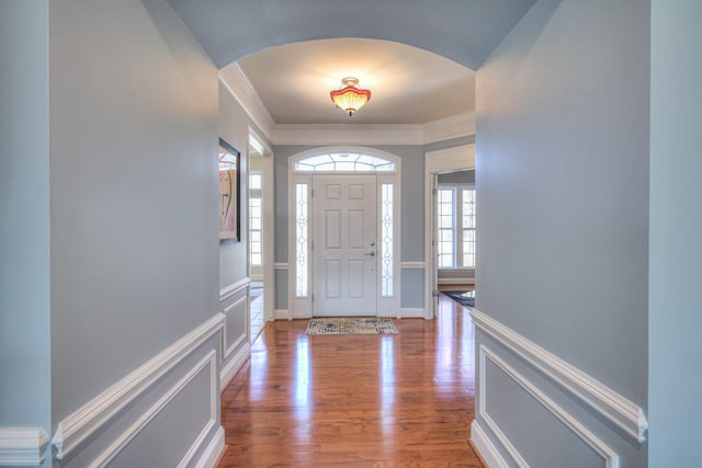 entryway featuring arched walkways, wood finished floors, crown molding, and a decorative wall