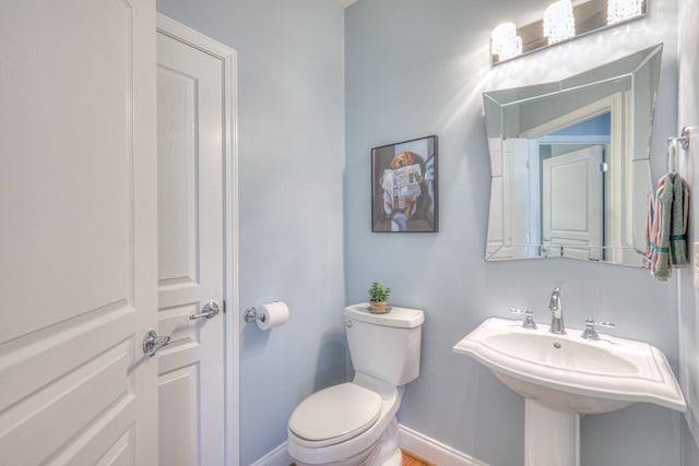 half bathroom featuring toilet, baseboards, and a sink