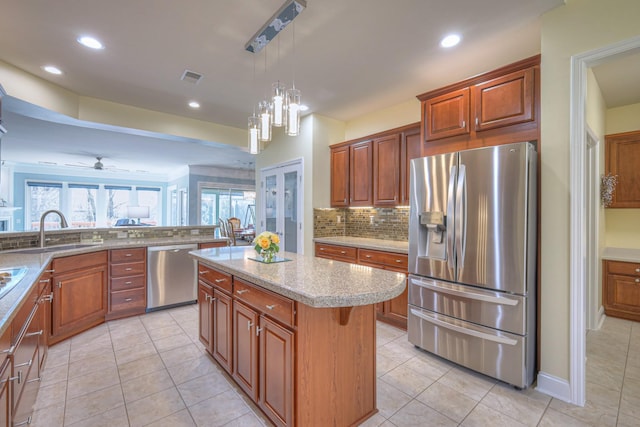 kitchen with visible vents, a kitchen island, a sink, stainless steel appliances, and tasteful backsplash