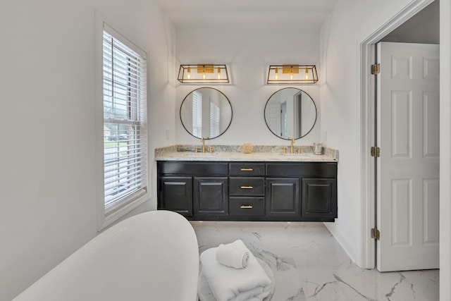 full bath with a sink, a freestanding bath, marble finish floor, and double vanity