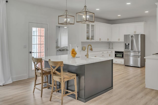 kitchen featuring white cabinets, glass insert cabinets, appliances with stainless steel finishes, light wood-type flooring, and backsplash