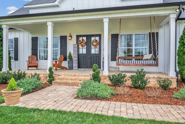 entrance to property with a porch, board and batten siding, and roof with shingles