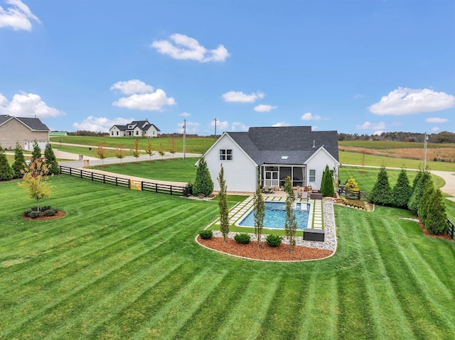 rear view of property featuring a rural view, a lawn, fence, and a sunroom