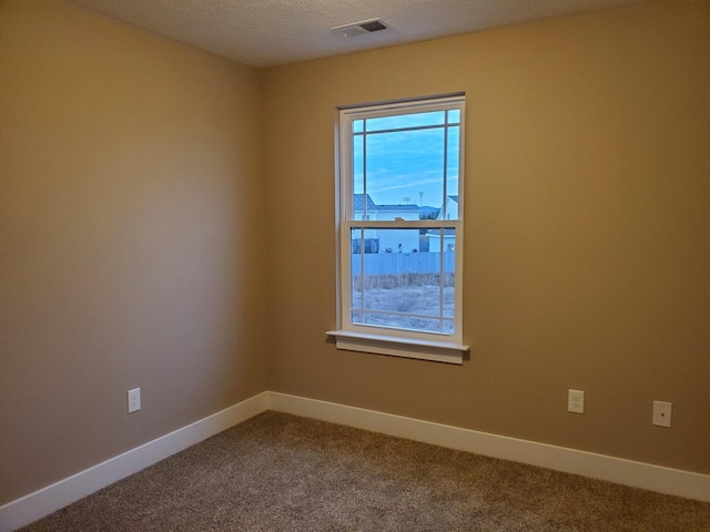 empty room featuring visible vents, baseboards, dark colored carpet, and a textured ceiling