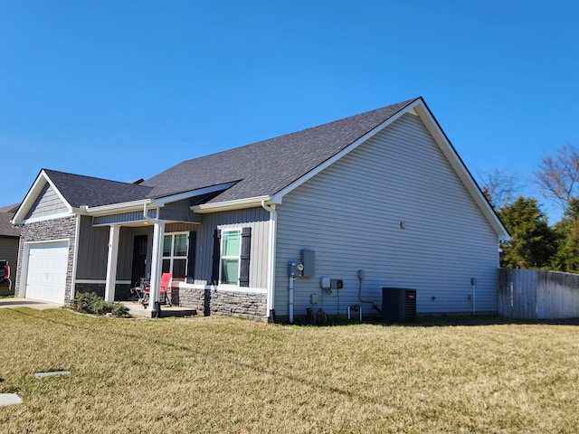 view of home's exterior with stone siding, a lawn, central AC unit, and an attached garage