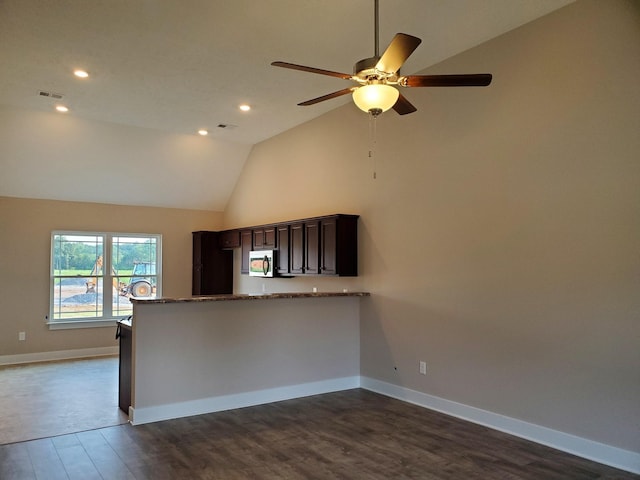 kitchen featuring high vaulted ceiling, stainless steel microwave, stone counters, baseboards, and dark wood-style flooring