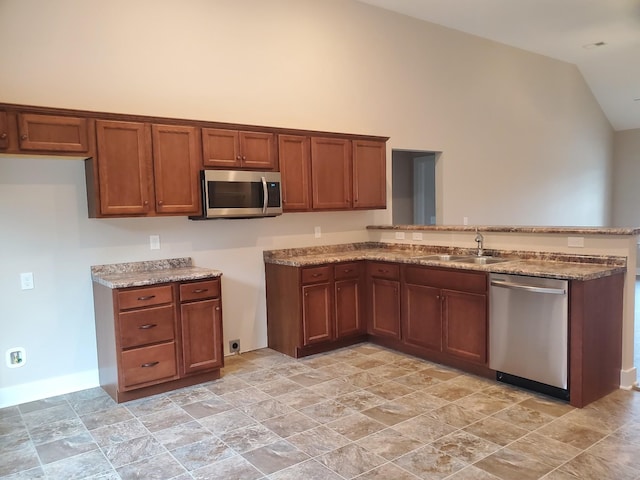 kitchen with light stone counters, brown cabinetry, a peninsula, a sink, and stainless steel appliances