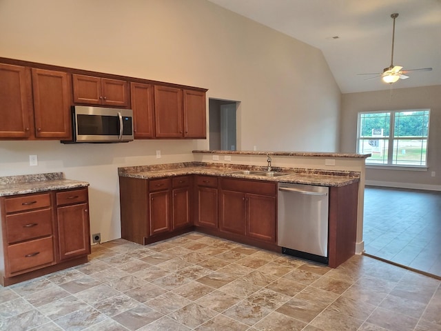 kitchen with a sink, light stone counters, stainless steel appliances, a peninsula, and brown cabinetry