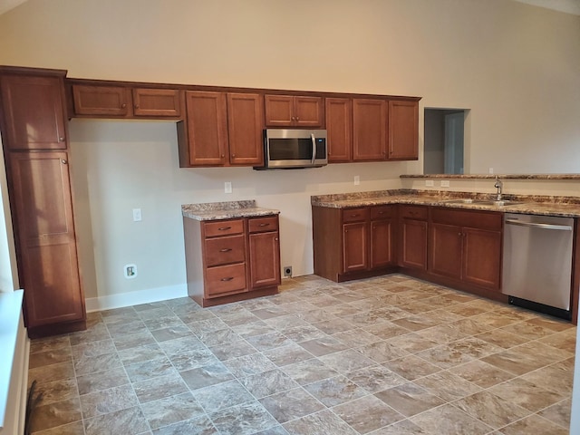 kitchen featuring light stone counters, appliances with stainless steel finishes, a high ceiling, brown cabinetry, and a sink