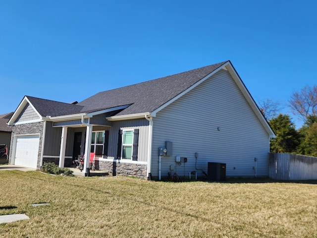 view of home's exterior with stone siding, an attached garage, a yard, and fence