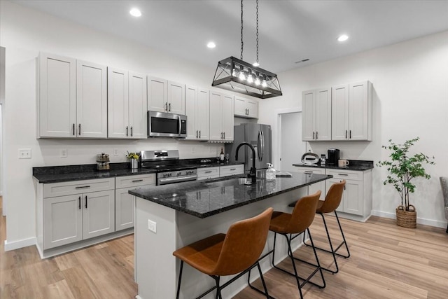 kitchen featuring appliances with stainless steel finishes, a kitchen bar, light wood-style floors, and a sink