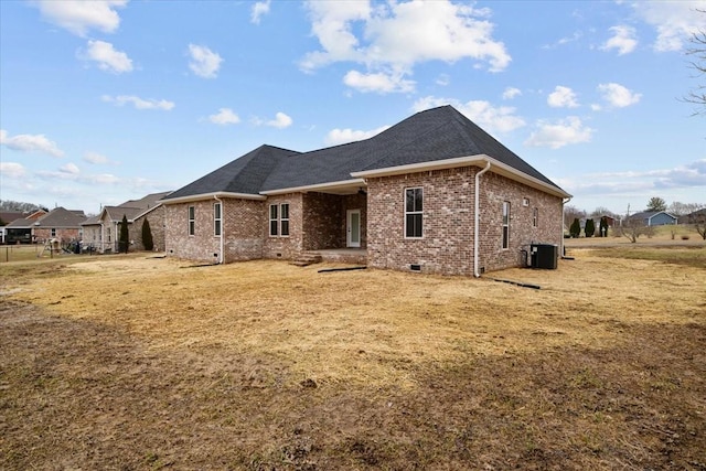 rear view of property featuring a lawn, central AC, a shingled roof, crawl space, and brick siding