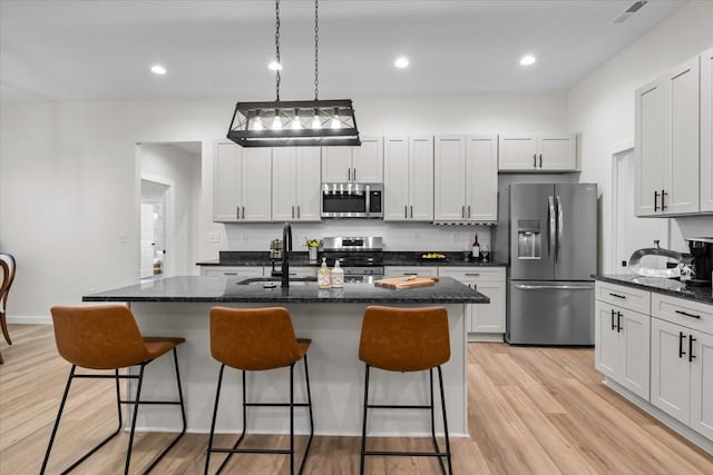 kitchen featuring light wood-type flooring, visible vents, a sink, stainless steel appliances, and a breakfast bar area