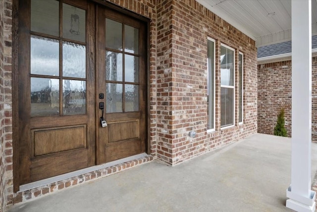 doorway to property with brick siding, covered porch, french doors, and a shingled roof