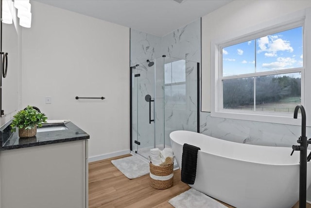 bathroom featuring vanity, wood finished floors, a marble finish shower, a freestanding tub, and tile walls