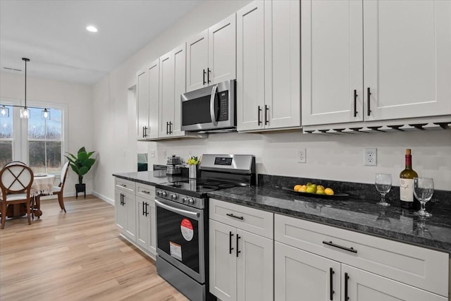 kitchen featuring dark stone countertops, stainless steel appliances, light wood-style floors, baseboards, and hanging light fixtures