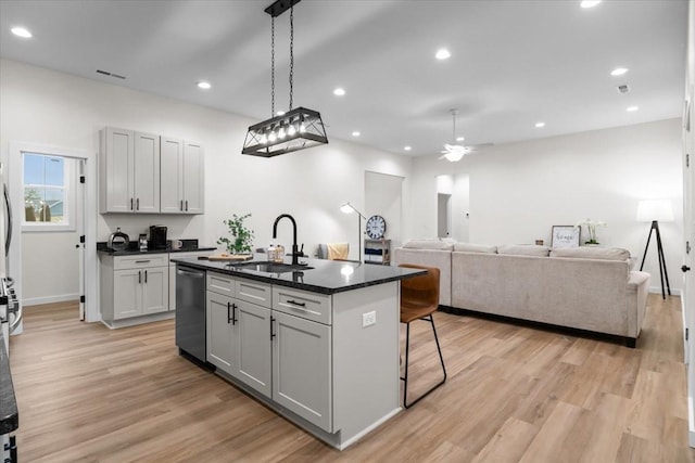 kitchen featuring a sink, dishwashing machine, light wood-type flooring, and a kitchen island with sink