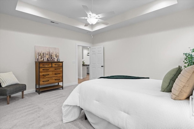 bedroom featuring visible vents, baseboards, a raised ceiling, light colored carpet, and ceiling fan