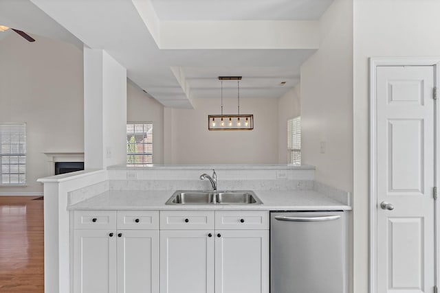 kitchen featuring wood finished floors, a fireplace, a sink, white cabinets, and stainless steel dishwasher