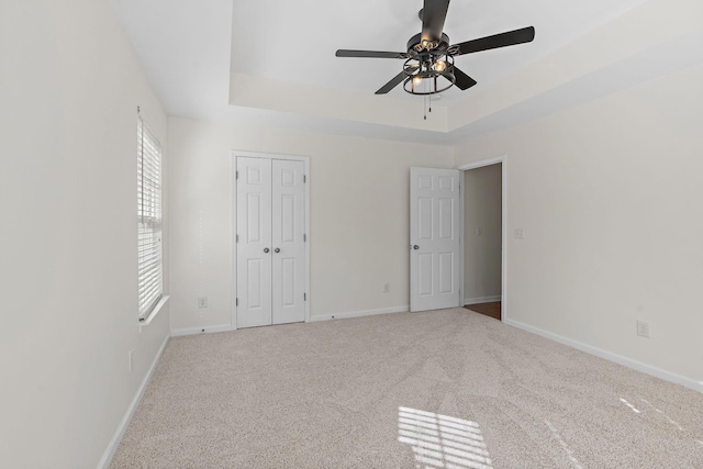 unfurnished bedroom featuring baseboards, carpet flooring, a closet, a raised ceiling, and a ceiling fan