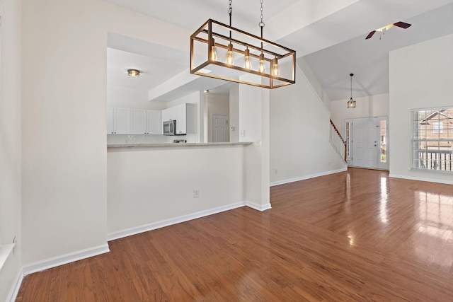 interior space featuring ceiling fan with notable chandelier, stainless steel microwave, wood finished floors, white cabinets, and baseboards