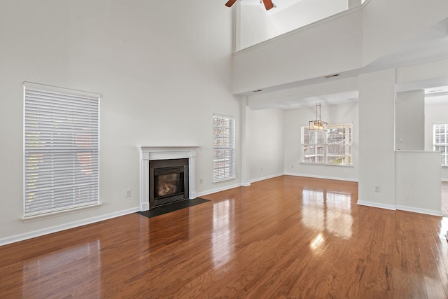 unfurnished living room featuring baseboards, a fireplace with flush hearth, a high ceiling, wood finished floors, and a ceiling fan