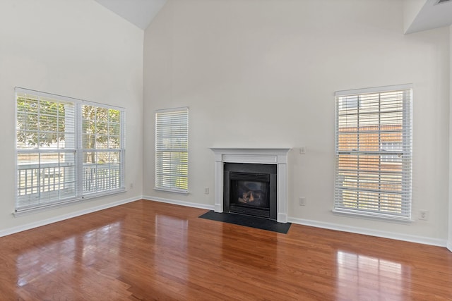 unfurnished living room featuring baseboards, a fireplace with flush hearth, high vaulted ceiling, and wood finished floors