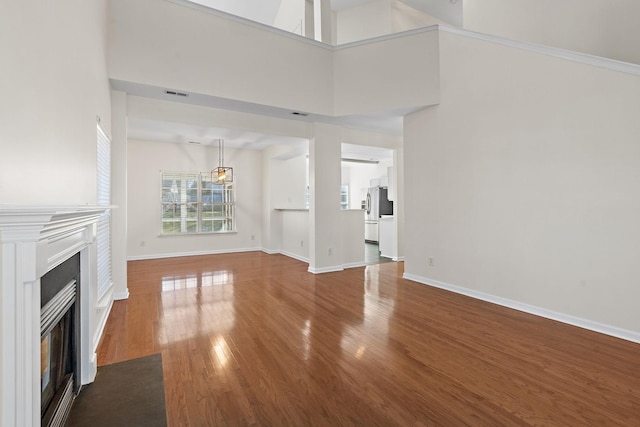 unfurnished living room featuring a fireplace with flush hearth, baseboards, visible vents, and wood finished floors