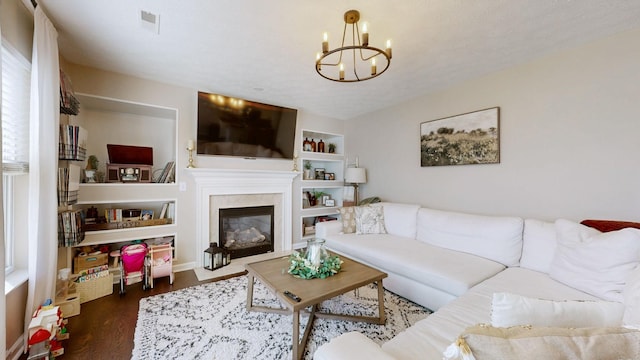 living room featuring visible vents, a chandelier, built in features, a fireplace, and wood finished floors